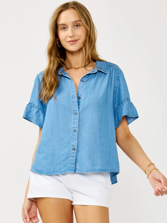 Woman wearing a blue denim shirt and white shorts on a plain background