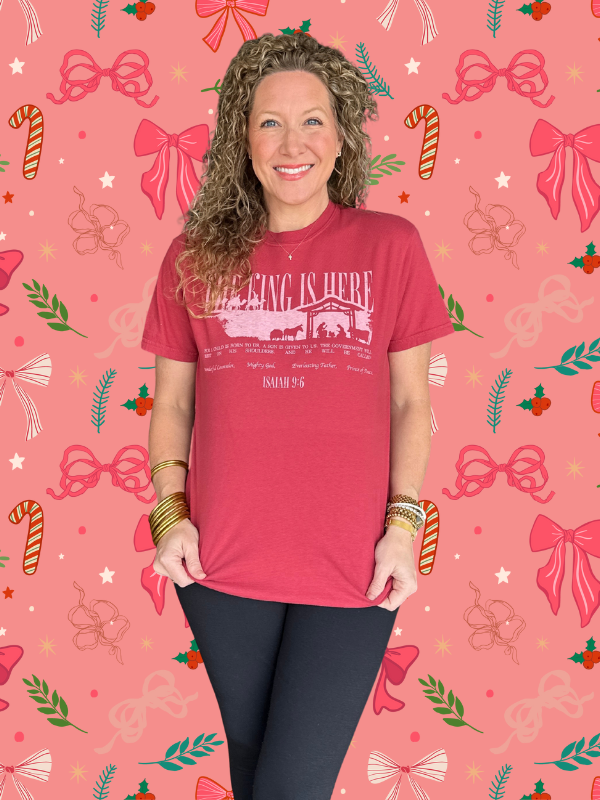 Woman wearing a red t-shirt with text on a pink background with festive designs