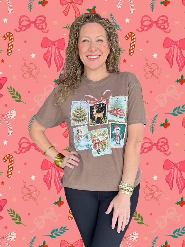 Woman wearing a brown t-shirt with vintage-style Christmas card designs on a pink background with festive decorations.