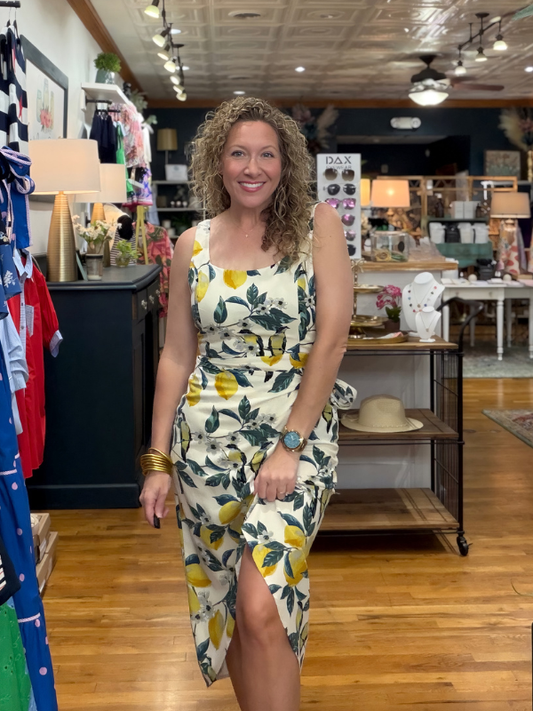 Woman in a lemon-patterned dress standing in a store with clothing racks and displays.