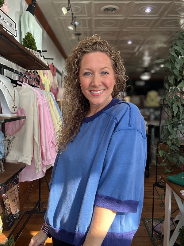 Woman wearing a blue shirt in a store setting with racks of clothes and decor.