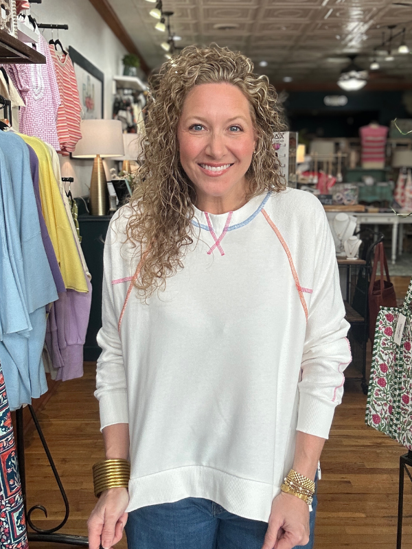 Woman wearing a white sweatshirt with colorful accents in a clothing store.
