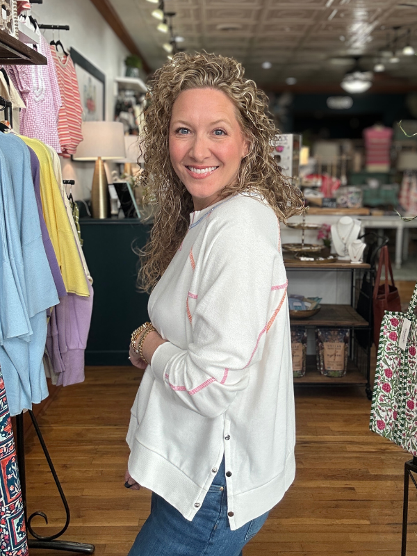 Woman in a white sweater with colorful accents standing in a clothing store.