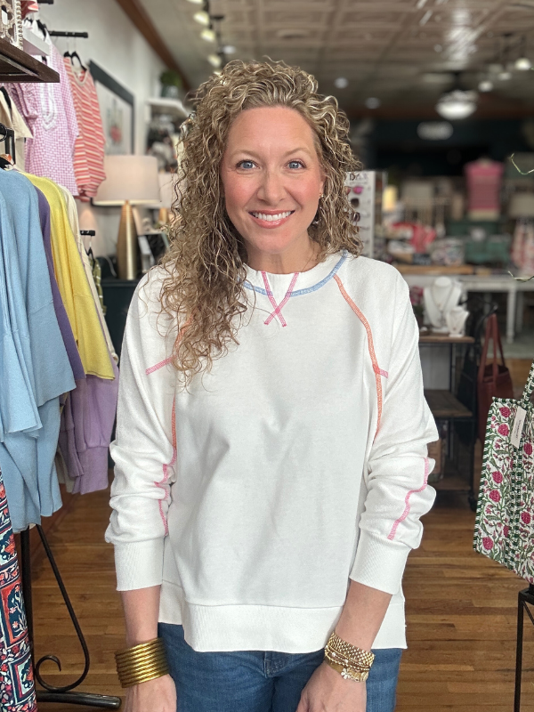 Woman wearing a white sweatshirt with colorful accents in a clothing store.