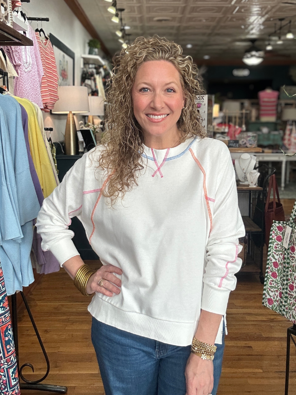 Woman wearing a white sweatshirt with colorful accents in a clothing store.