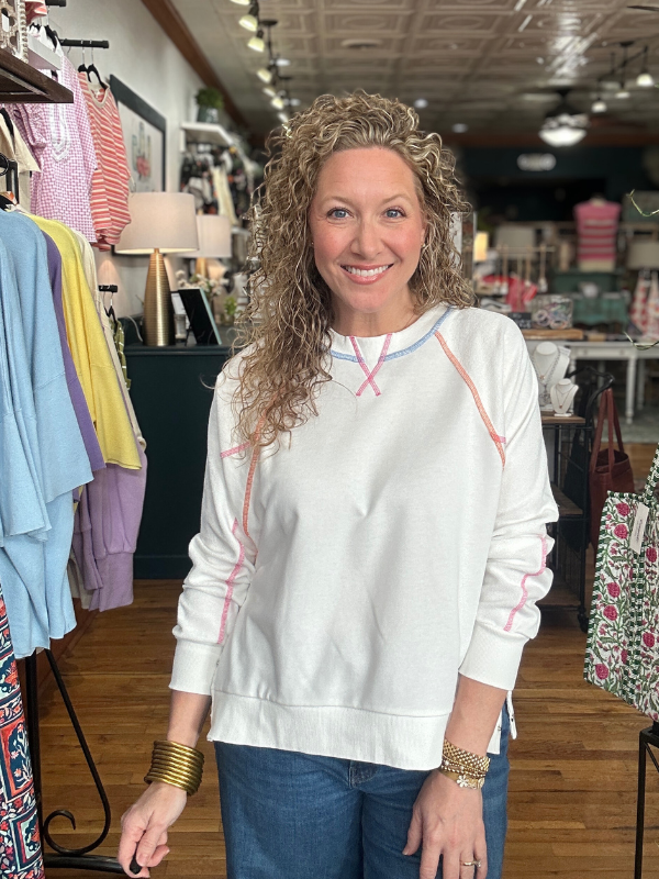 Woman wearing a white sweatshirt with colorful accents in a clothing store.