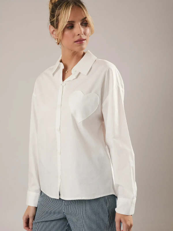Woman wearing a white blouse with a heart detail on a plain background
