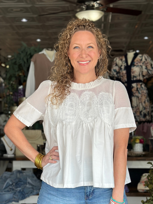 Woman wearing a white blouse with lace details in a clothing store.