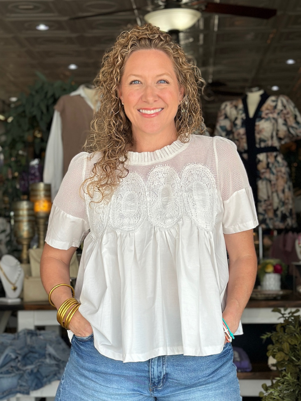 Woman wearing a white blouse with lace details and blue jeans in a store setting.