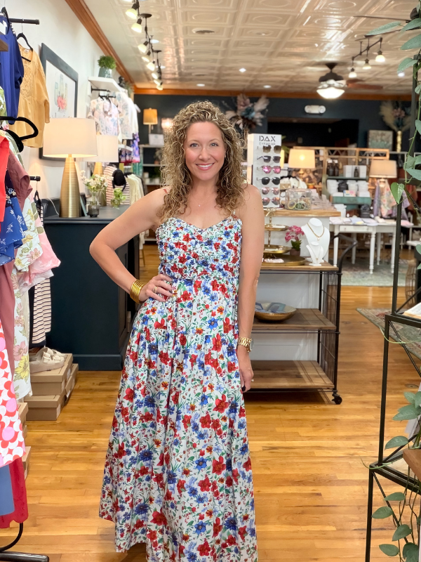 Woman in a floral dress standing in a store with various items on shelves and tables.