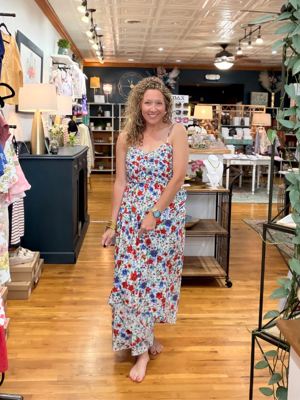 Woman in a floral dress standing in a store with wooden floors and shelves.