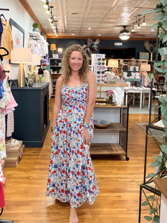 Woman in a floral dress standing in a store with clothing racks and displays.