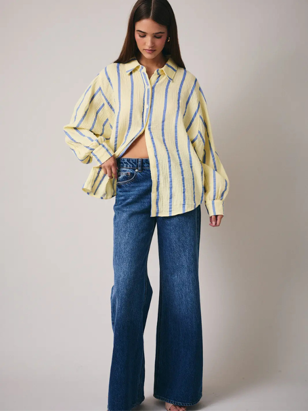 Woman wearing a yellow and blue striped shirt and blue jeans against a plain background