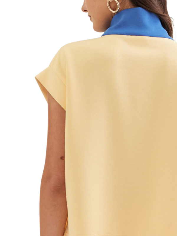 Yellow top worn by a person with a blue collar visible over the shoulder on a white background