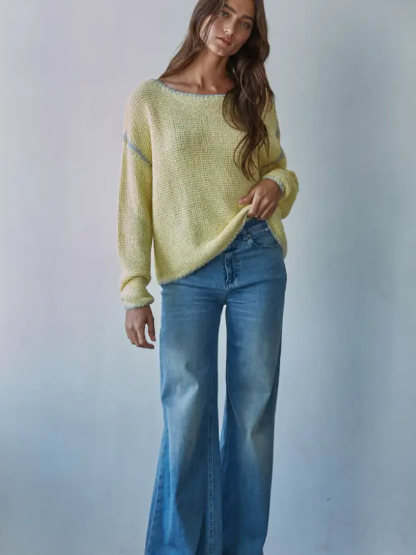 Woman wearing a yellow sweater and blue jeans against a plain background