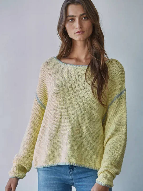Woman wearing a light green sweater with blue jeans against a plain background