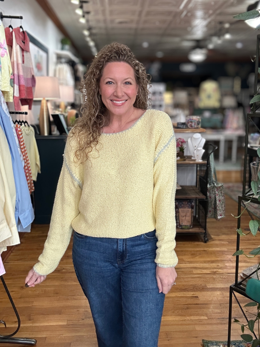 Woman wearing a yellow sweater and blue jeans standing in a store.